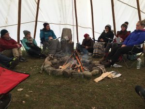 Class sitting around a fire in a tipi