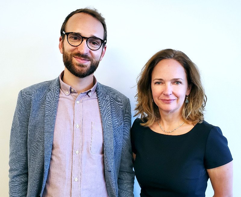 portrait of man with glasses and beard, jacket and button down shirt, next to woman with medium length hair and black scoop necked t shirt