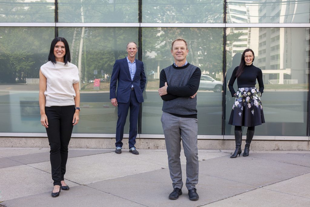 four people standing in front of a glass building