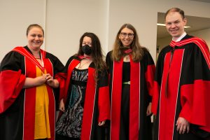 Four graduates pose for a photo during the Hooding Ceremony reception.