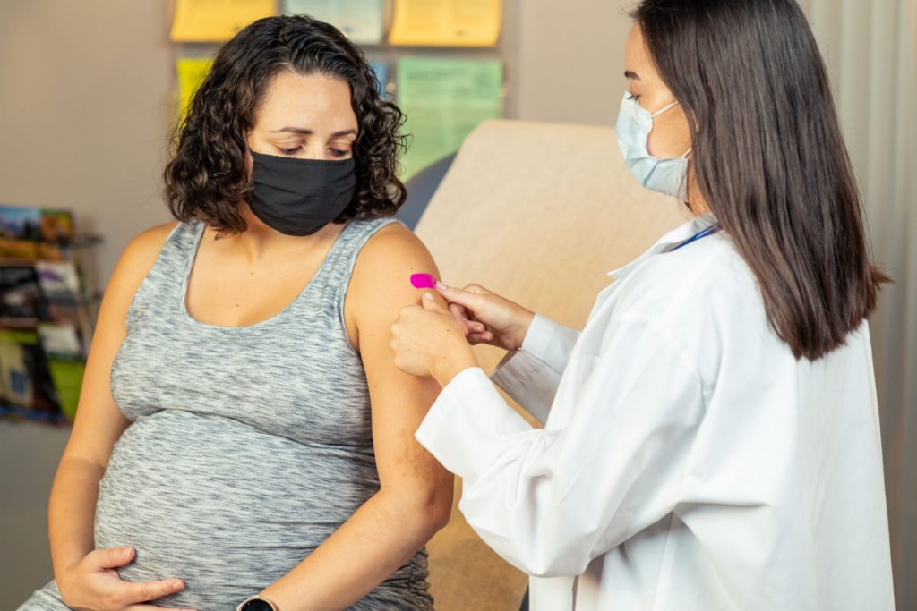 In this 2022 photo, captured inside a clinical setting, a health care provider places a bandage on the injection site of a pregnant patient who just received an influenza vaccine. The best way to prevent seasonal flu is to get vaccinated every year. Centers for Disease Control and Prevention (CDC) recommends everyone 6-months of age and older get a flu vaccine every season.
