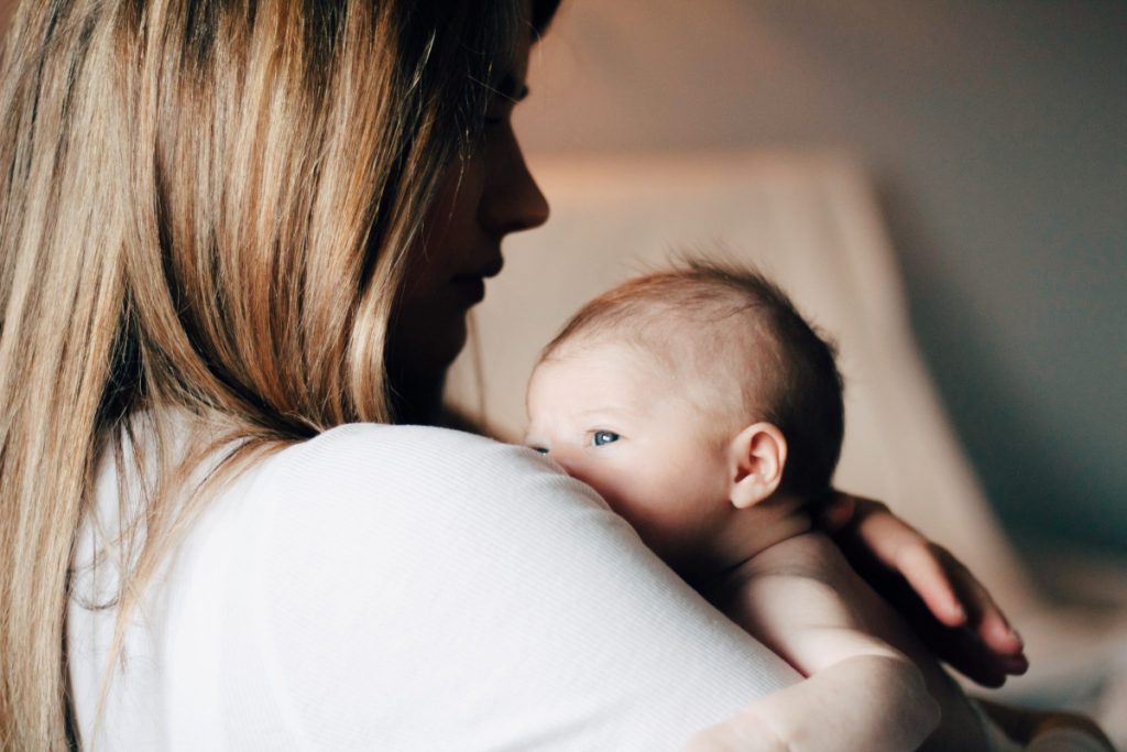 Woman with long hair holding a young baby over her shoulder. (Upsplash)