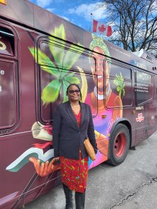 Dr. Roberta K Timothy stands before a TTC bus with her image on the bus for Black History Month